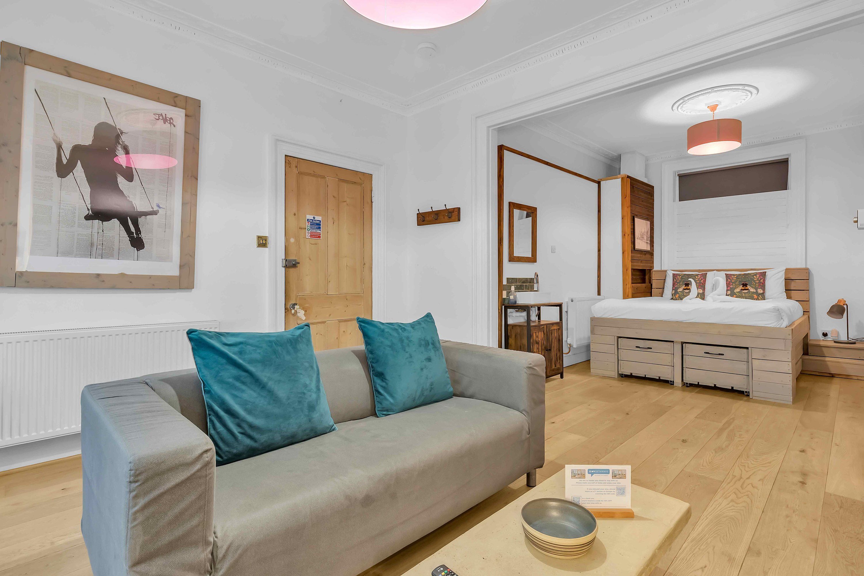 Ein modernes Wohnzimmer mit einem grauen Sofa, Türkis-farbenen Kissen, einem Holztisch und einem Gemälde an der Wand.