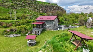 A stone building with a red roof, surrounded by lush greenery and a rocky hillside.