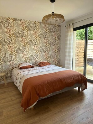 Ein Schlafzimmer mit strukturierter Tapete, einem Bett mit brauner Bettdecke, Holzboden und einer Hängeleuchte.