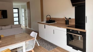 A modern kitchen with a wooden countertop, a black stove, and a white cabinet. There is a dining area with a table and chairs. - Le Balleré - Gîtes du Bessin (Balleroy-sur-Drôme)