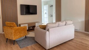 A modern living room with a sofa, a TV, and a wooden floor. - Le Balleré - Gîtes du Bessin (Balleroy-sur-Drôme)