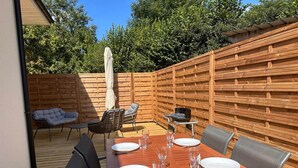 An outdoor dining area with a wooden table set for four, surrounded by chairs, and a wooden fence in the background. - Le Balleré - Gîtes du Bessin (Balleroy-sur-Drôme)