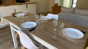 A dining table set with white plates, cutlery, and wine glasses, surrounded by white chairs in a modern kitchen and living area. - Ce logement vous accueille à 25mn des plages des sites du D-DAY et de ses plages (Balleroy-sur-Drôme)