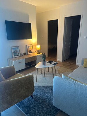 A modern living room with a flat-screen TV mounted on the wall, a small table with a lamp, and a sofa.