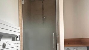 A compact bathroom with a glass shower enclosure, a built-in washing machine, and a patterned floor mat. - Ce logement vous accueille à 25mn des plages des sites du D-DAY et de ses plages (Balleroy-sur-Drôme)
