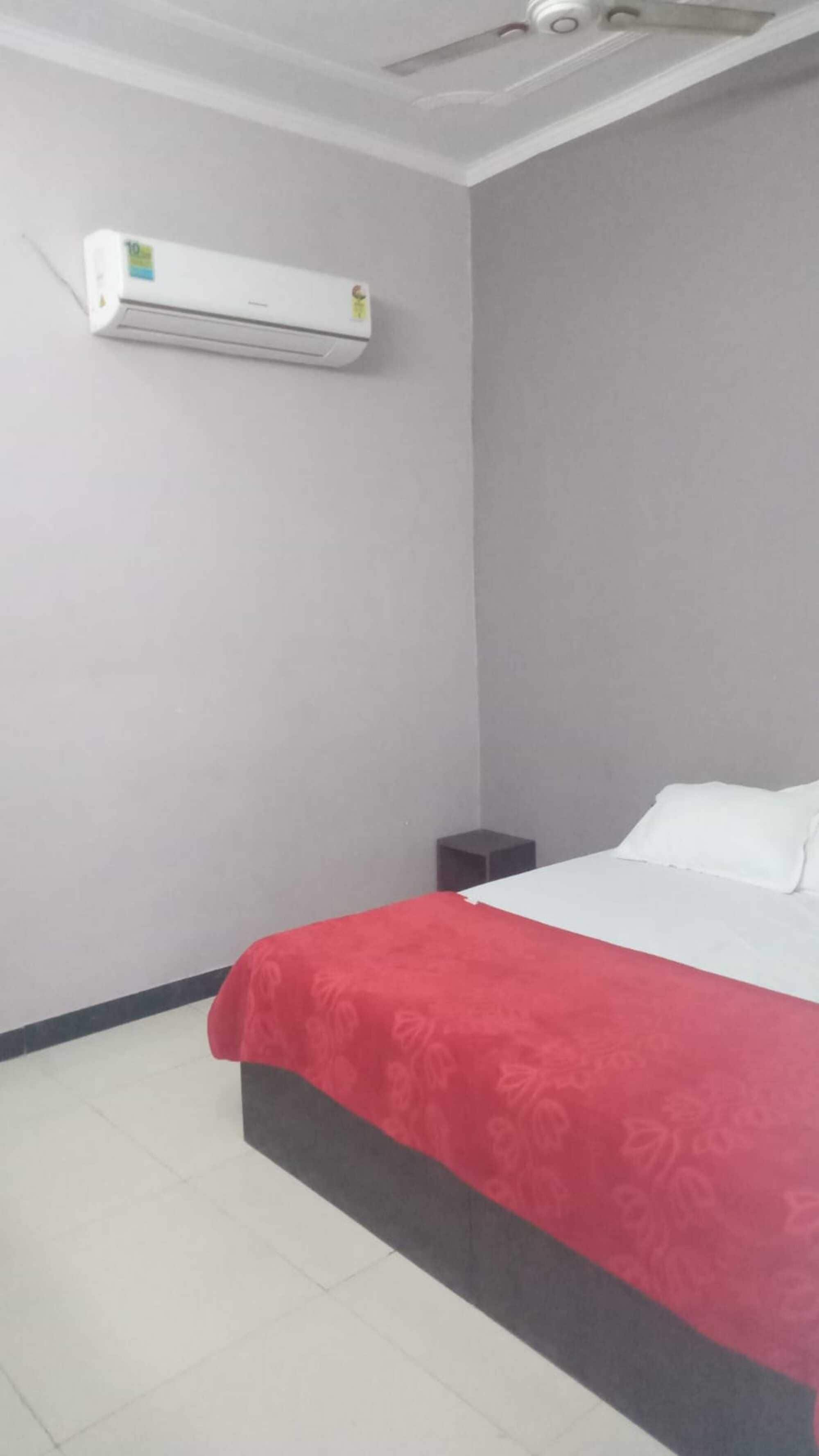 A bedroom with a bed, a nightstand, a wall-mounted air conditioner, and a ceiling fan.