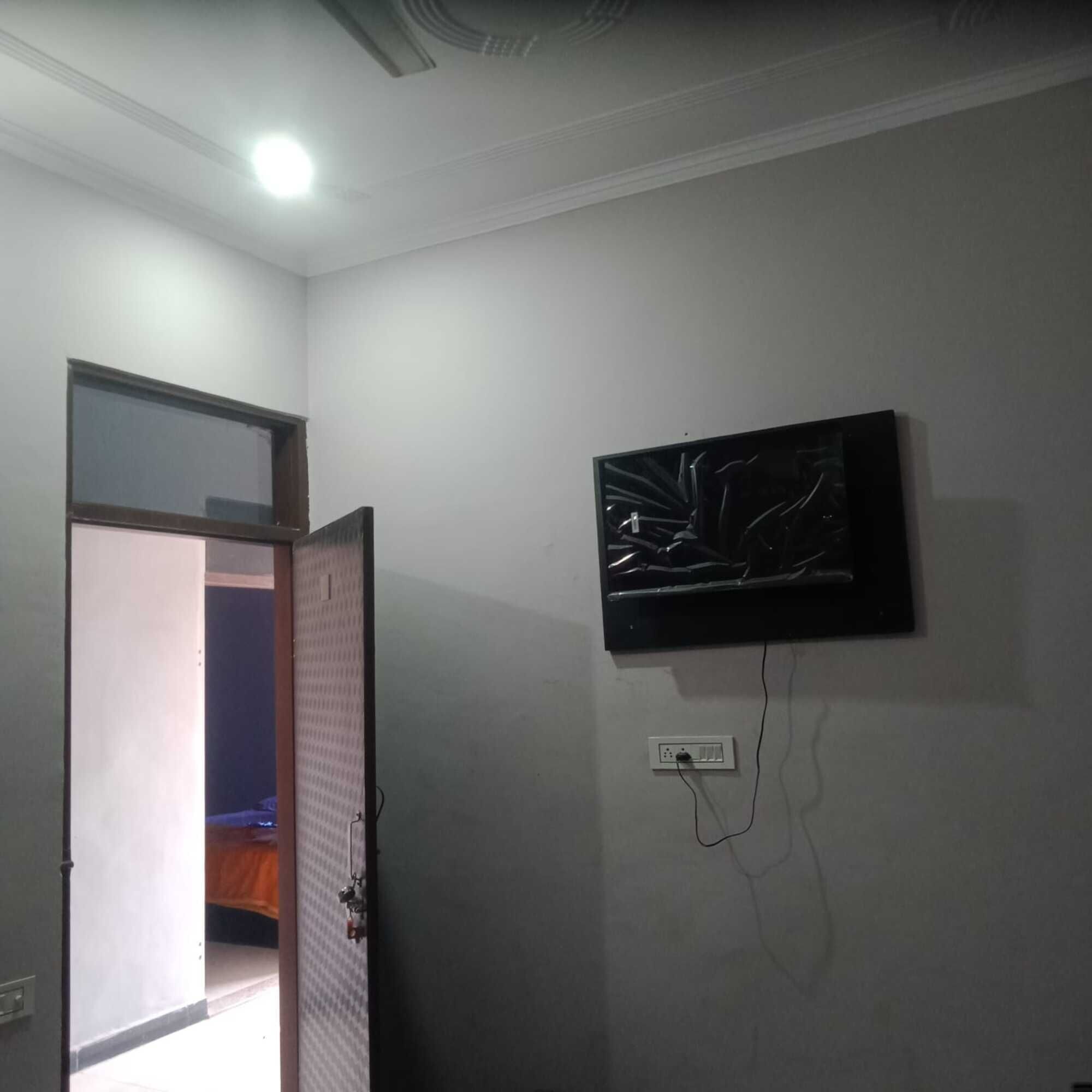 A room with a television mounted on the wall, a door leading to another room, and a ceiling light.