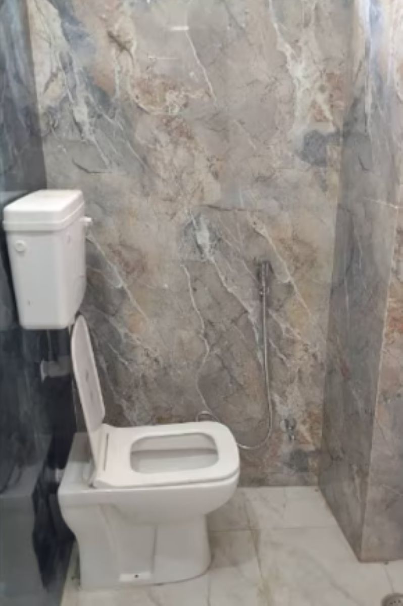 A bathroom with a toilet, marble walls, and a visible plumbing fixture.