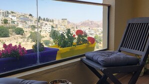 A balcony with a view of a cityscape, a wooden stool, a chair, and flower planters. - Petra Masterpiece  (Wadi Musa)