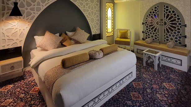 A modern bedroom with a large bed, a small sofa, a decorative wall, and a patterned carpet. - Petra Masterpiece  (Wadi Musa)