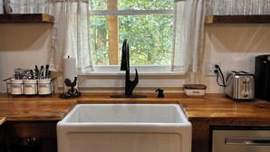 Una cocina con un lavamanos blanco, armarios de madera, una ventana con cortinas y un tostador sobre la encimera.
