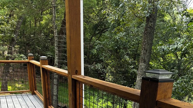 Una terraza de madera con barandilla metálica que da a un área boscosa.
