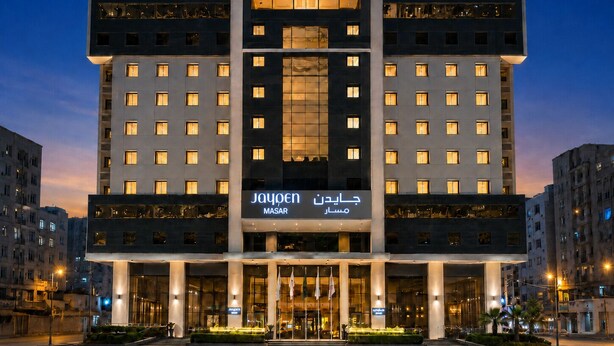 Un hotel moderno con una entrada central, varios pisos y ventanas iluminadas.