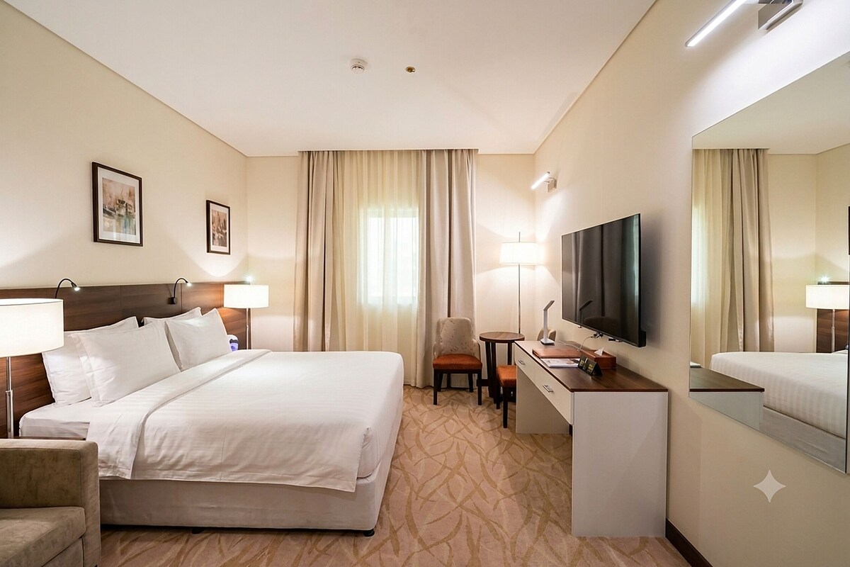Una habitación de hotel con cama, escritorio, silla, televisor y espejo.