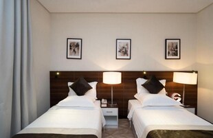 Habitación de hotel con dos camas, cabecero de madera, lámparas de noche, mesitas de noche y tres cuadros enmarcados en la pared.