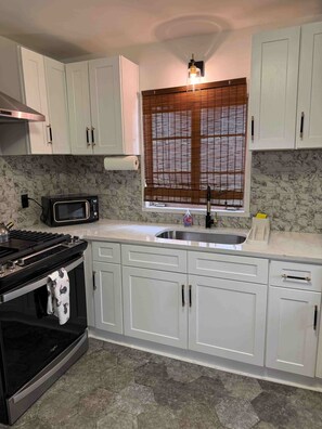 A kitchen with white cabinets, a black stove, a microwave, a sink, and a window with blinds. - Mary’s Ranch Retreat! Your Home away from Home! (Atlanta)