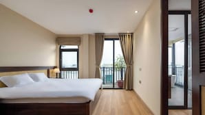 A hotel room with a large bed, a window with curtains, a balcony with a potted plant, and a view of the city. - Westlake High Floor (Hanoi)