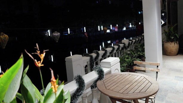 A balcony with a wooden table and chairs, white balustrades, and potted plants. - Westlake High Floor (Hanoi)
