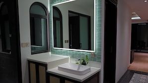 A modern bathroom with a white sink, a large mirror, and a green-tiled wall. - Westlake High Floor (Hanoi)
