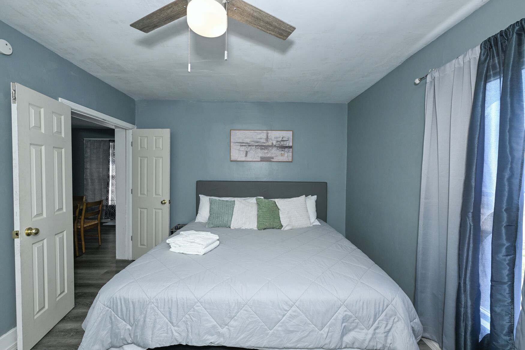 Une chambre à coucher avec un lit, un ventilateur de plafond, une porte et une fenêtre avec des rideaux.