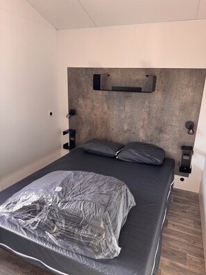 A bedroom with a bed, a headboard, bedside tables, and a wall-mounted light fixture.