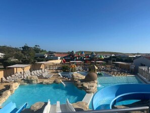 A pool area with lounge chairs, a water slide, and a view of the surrounding landscape. - Spacious, air-conditioned mobile home at Sol a Gogo Campground (Saint-Hilaire-de-Riez)