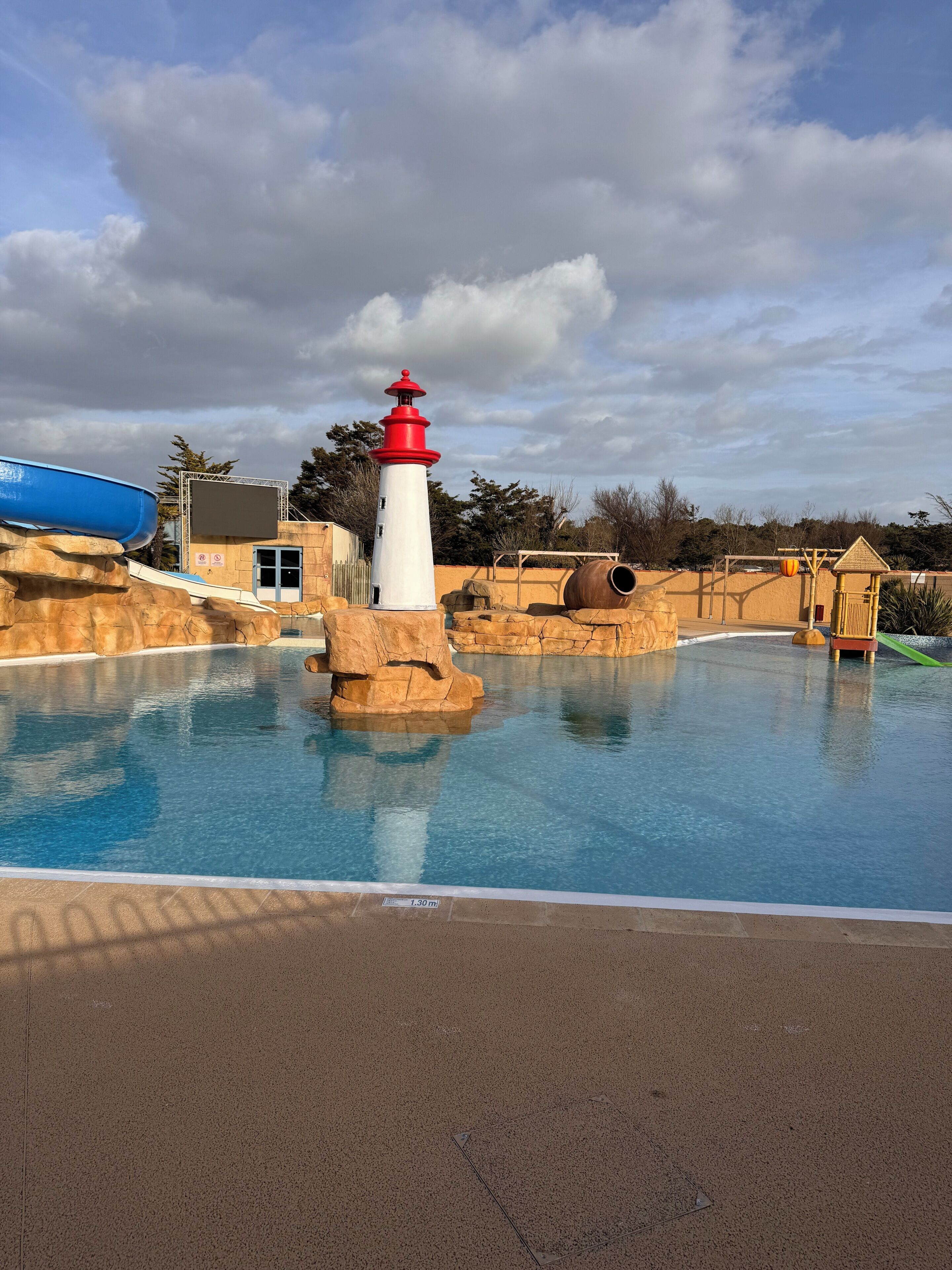 A swimming pool with a lighthouse structure, a slide, and a rock formation.