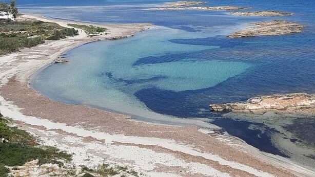 Een kustlandschap met helderblauw water, zandstranden en rotsachtige rotsen.