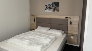 A neatly made bed with a white comforter and pillows, a wooden headboard, and a wall-mounted light fixture. - 150m from ski slopes, 2nd floor, swimming pool, tv, ski locker, 57m², Gourette (Eaux-Bonnes)