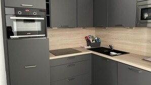 A modern kitchen with grey cabinetry, a built-in oven, a sink, and a countertop with a cutting board and utensils. - 150m from ski slopes, 2nd floor, swimming pool, tv, ski locker, 57m², Gourette (Eaux-Bonnes)