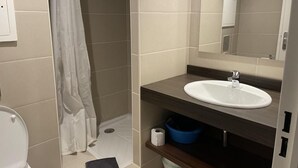 Et badeværelse med brusebad, toilet, vask og spejl.