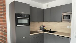 Een moderne keuken met grijze kastjes, een zwarte oven, een magnetron en een houten aanrecht.