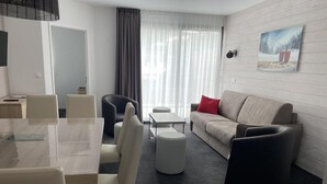 A modern hotel room with a dining area, a sofa, and a painting on the wall.