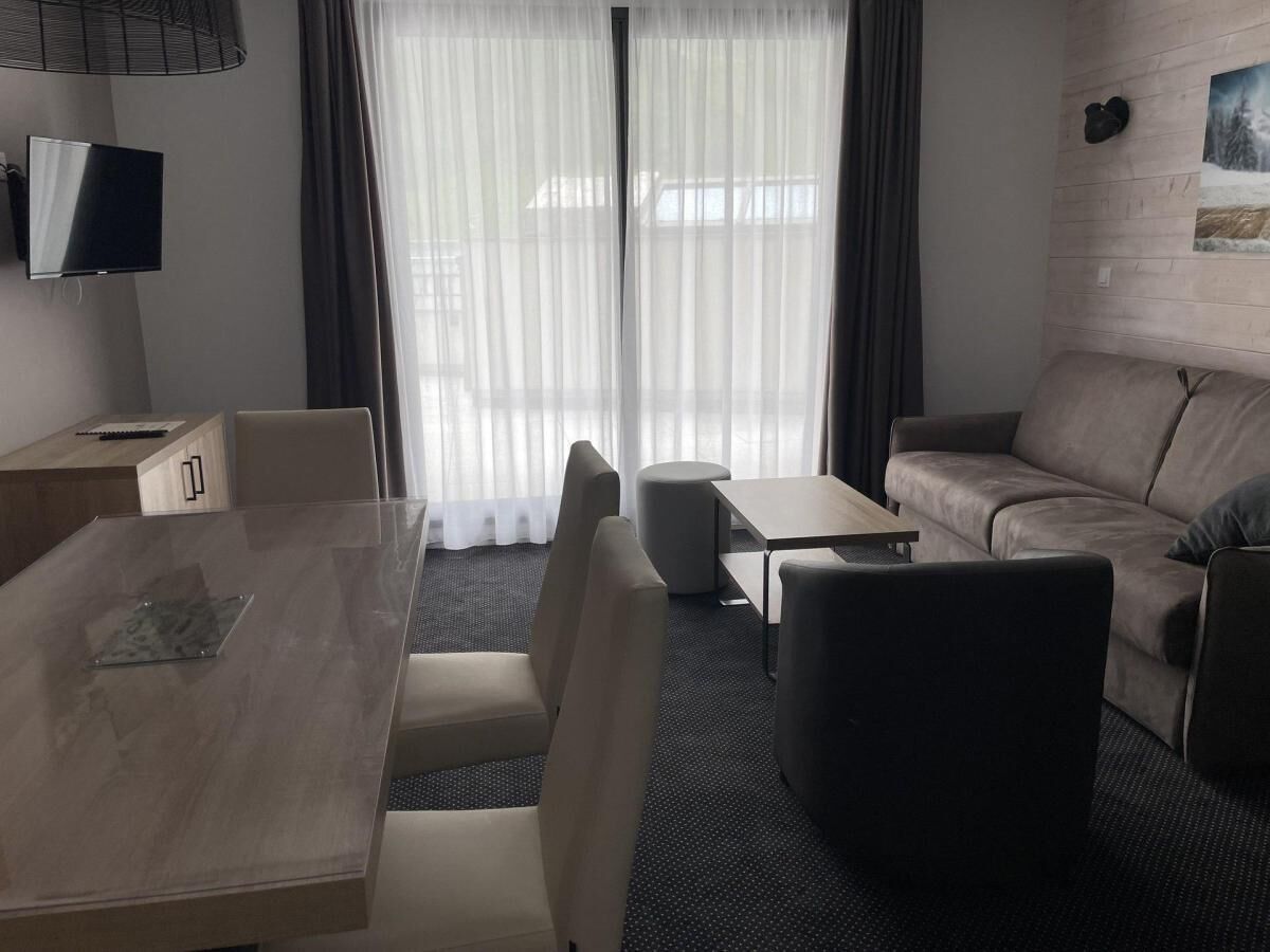 A modern hotel room with a dining table, two chairs, a sofa, a small table, and a TV.