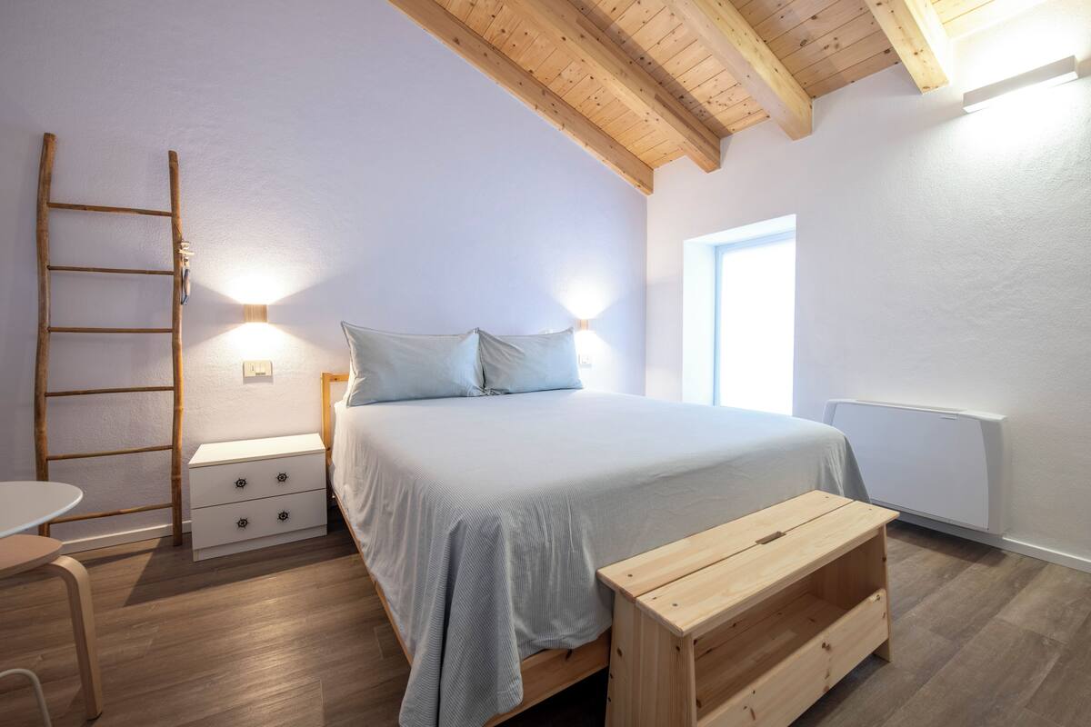 A bedroom with a wooden bed, bedside tables, a wooden bench, a ladder, and a window.