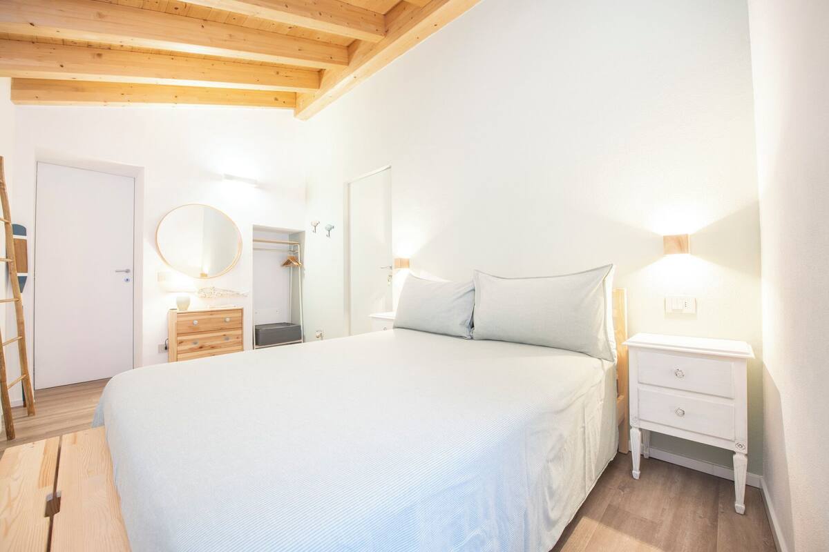 A bedroom with a large bed, wooden headboard, bedside tables with lamps, a wardrobe, and a mirror.