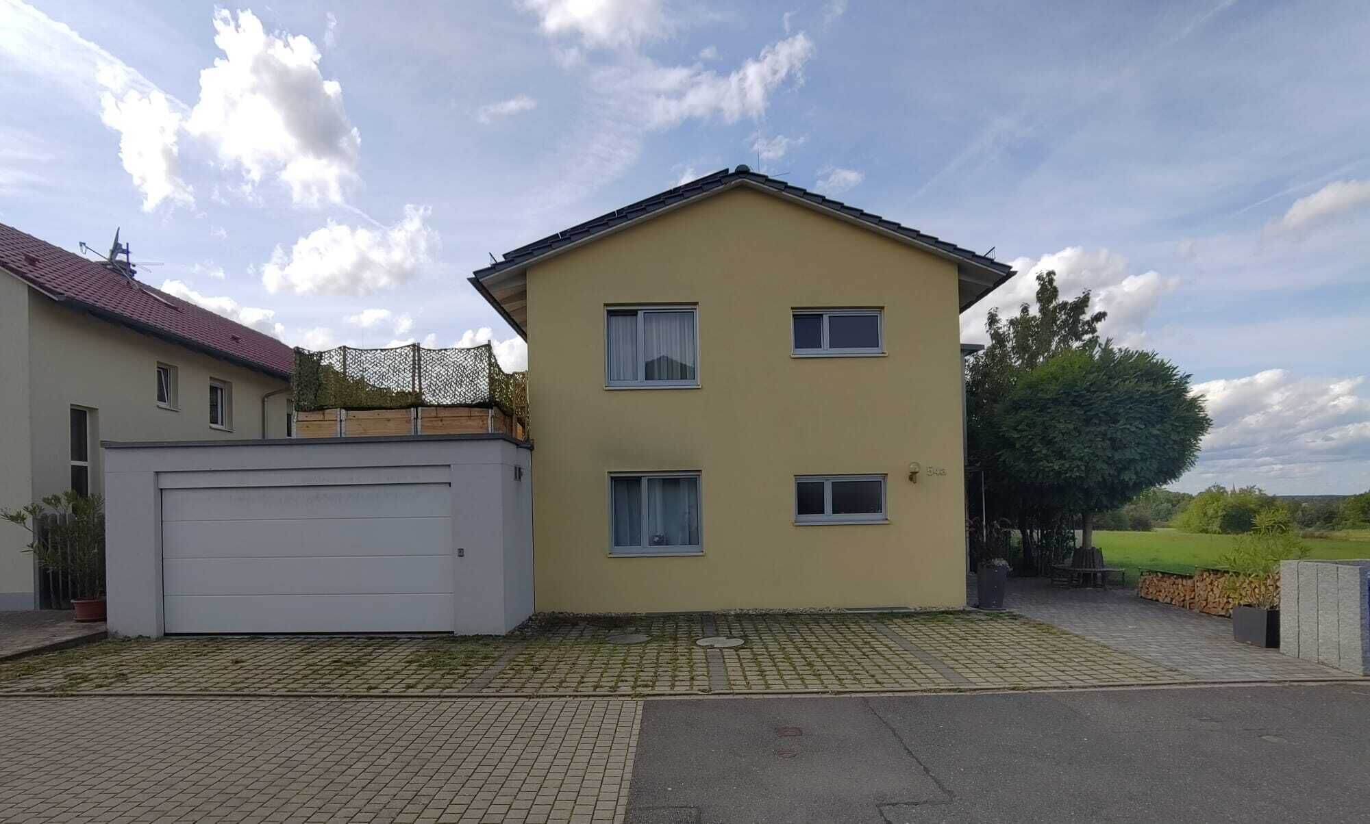 Ein zweistöckiges Wohnhaus mit Garage, umzäunter Garten und gepflasterter Auffahrt.