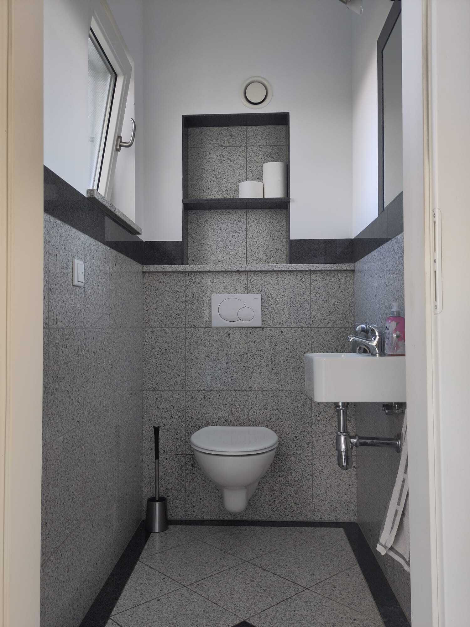 Ein kleines Badezimmer mit Toilette, Waschbecken und Ablagefach.