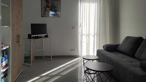 Ein modernes Wohnzimmer mit grauem Sofa, einem kleinen runden Tisch, einem Fernseher auf einem Schrank und einem Bild an der Wand.