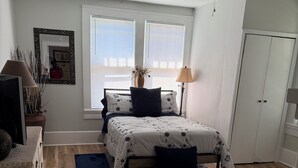 Una camera da letto con un letto, una ventola a soffitto, una finestra con persiane, un comodino, una lampada e un armadio.