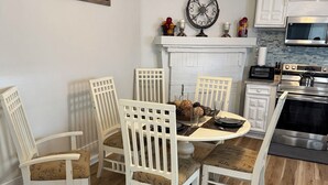 Zona pranzo con un tavolo rotondo, quattro sedie bianche e un elemento decorativo a parete.