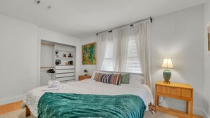 A bedroom with a bed, a bedside table with a lamp, a wardrobe, and a painting on the wall.