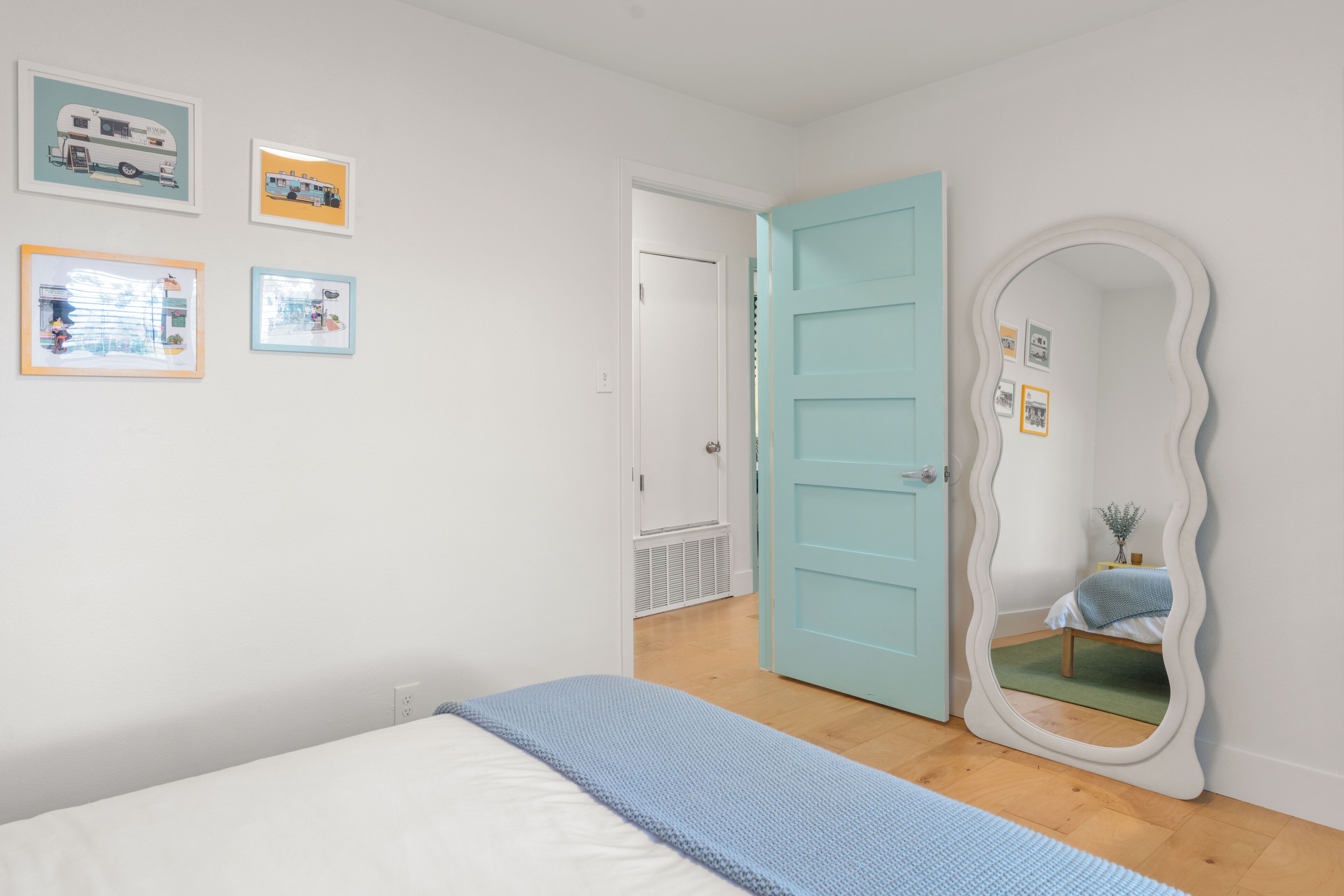 Un dormitorio con una cama, una puerta azul, un espejo y decoración en la pared.