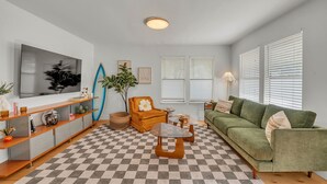 A living room with a checkered floor, a green sofa, a wooden coffee table, a television, and a surfboard.