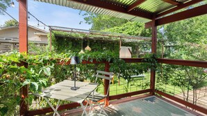 Un porche cubierto con una mesa y sillas, rodeado de vegetación y vistas al jardín trasero.