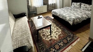 A furnished room with a bed, a sofa, a coffee table, and a patterned rug. - Grandi Suit Pansiyon (Elazığ)