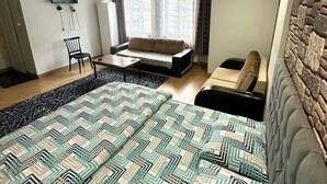 A modern bedroom with a large bed, a sofa, a TV, and a window with curtains. - Grandi Suit Pansiyon (Elazığ)