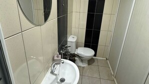 A compact bathroom with a white sink, a round mirror, a toilet, and a black-tiled wall. - Grandi Suit Pansiyon (Elazığ)