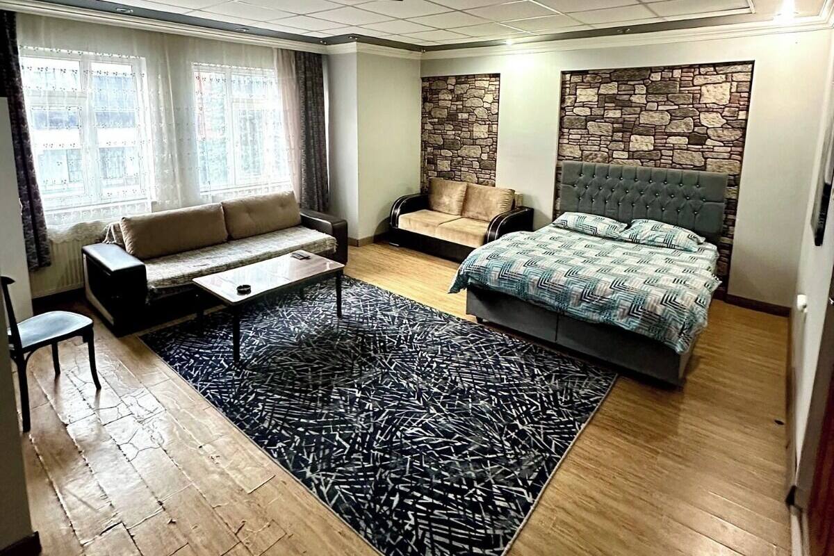 A modern bedroom with a large bed, a sofa, a small table, and a stone accent wall.