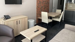 A modern hotel room with a flat-screen TV mounted on the wall, a wooden cabinet with a phone, a dining table with chairs, a sofa, and a kitchen area with a microwave. - 150m from ski slopes, 3rd floor, view mountain, swimming pool, terrace, tv, ski locker, 28m² (Eaux-Bonnes)